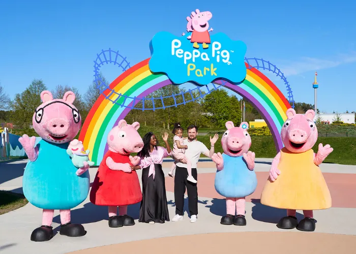 Familie mit Kind posiert vor einem bunten Regenbogentor mit dem Schriftzug 'Peppa Pig Park'